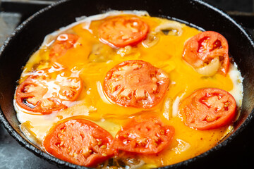 Eggs with tomatoes and onions in a pan are fried in oil