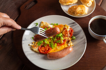 Eggs with tomatoes and sausage in a plate on the table of coffee and a croissant of sausage