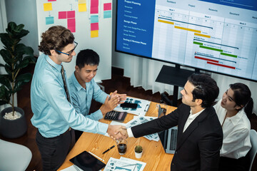 Cheerful meeting room, businesspeople celebrate with handshaking. Successful project was completed before the deadline. Business partnership and collaboration in project management. Meticulous