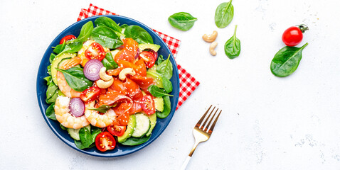 Seafood salad with shrimp, salmon, avocado, spinach, cucumber, tomato, cashew and sesame seeds.. White background, top view