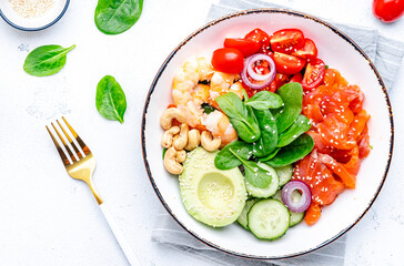 Seafood salad poke bowl with shrimp, salmon, avocado, spinach, cucumber, tomato, cashew, sesame seeds. White background, top view