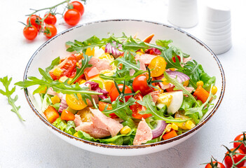 Tasty tuna vegetable salad with tomatoes, onion, corn, eggs, paprika, lettuce and arugula. White  background, top view