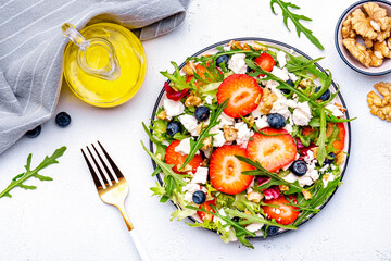 Strawberry and feta salad with arugula, lettuce, blueberries, cheese and walnuts, white background, top view