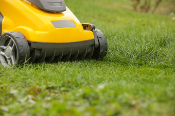 Yellow lawn mower on the spring green grass in the yard