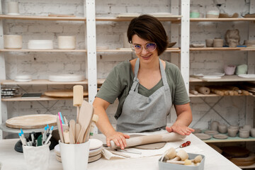 Slab building method in ceramics crafting. Using a wooden stick to roll out a flat sheet of clay. Preparing clay for cutting and assembling it.
