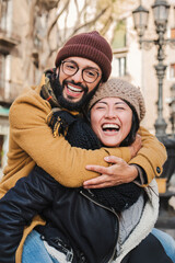 Vertical portrait. Young multiracial affectionate couple laughing and smiling together giving a piggyback ride, having fun embracing and hugging in a romantic date. Two friends bonding outdoors