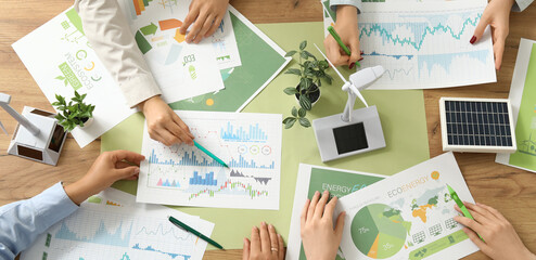 Business team with wind turbine models and solar panel during meeting in office. Green energy...