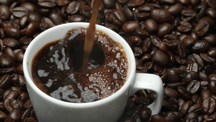 Freshly espresso was poured in white cup with pile of coffee bean. Pouring black coffee in the cup with brown background and seed scattering around on wooden table. Close up. Top view. Comestible.