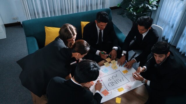 Top view of skilled businesswoman write marketing idea and placed sticky notes on mind mapping while planning financial strategy with diverse business group. Startup team working together. Directorate