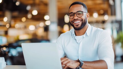 Obraz premium Smartly dressed man with glasses and a happy expression working on his laptop in a bright, contemporary office, representing professionalism and a positive work ethic.