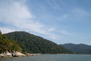 View of green mountains with rocks along the shore beside the sea.