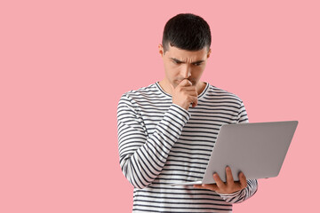 Thoughtful young man with laptop on pink  background