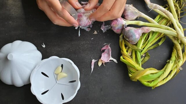 Hands peeling some garlics on black wooden table