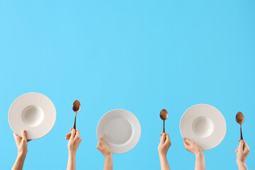 Female hands holding plates and spoons on blue background