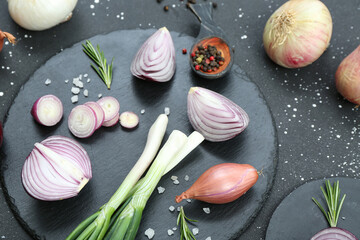 Boards with different kinds of onion on grunge black background
