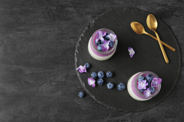 Glasses of panna cotta with blueberry and beautiful hydrangea flowers on black table