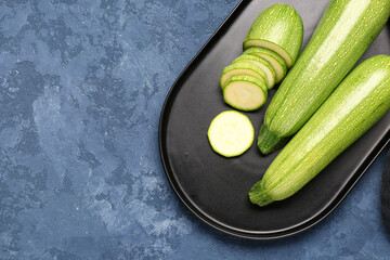 Tray with fresh green zucchini on blue background