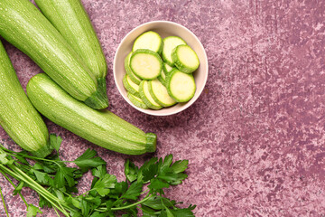 Many fresh green zucchini and bowl with slices on purple background