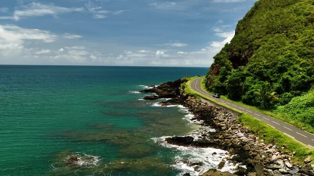 Aerial view of scenic tropical ocean and reef with a winding road along the rocky cliff, New Caledonia.