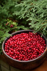 Wooden bowl of ripe juicy lingonberries on a wooden background