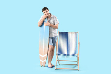 Obraz premium Young man with surfboard and deck chair on blue background