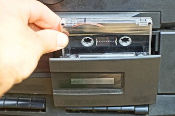 one plastic old stereo with a recording audio cassette with magnetic tape is inserted by hand into...