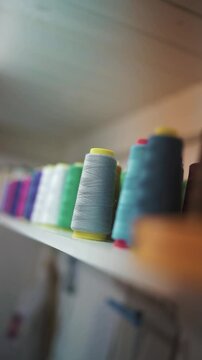 Vertical video of spools of thread on shelf in textile workshop. Colourful sewing supplies