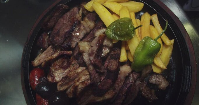 Beautiful slow motion shot of a grill plate as a chef places a padron bell pepper on top of the meat to serve at a fusion restaurant.