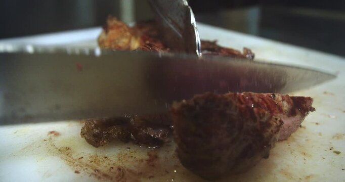 Beautiful slow motion shot of a tenderloin steak being cut with a knife on a table by a chef inside a restaurant kitchen.