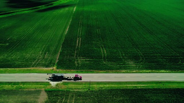 Red semi truck with RGN trailer, loaded with oversize load machinery in Indiana, USA. Aerial view.