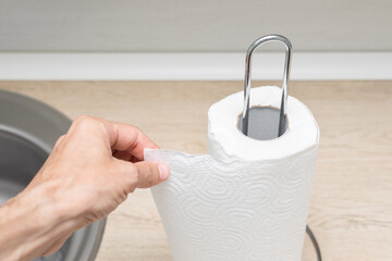 a man's hand tears off a piece of paper towel in the kitchen. using paper towel in the kitchen