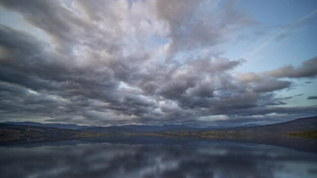 A dramatic sky filled with thick, rolling clouds over a calm body of water and distant mountains.