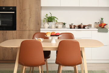 Stand with muffins and cinnamon rolls on wooden kitchen table