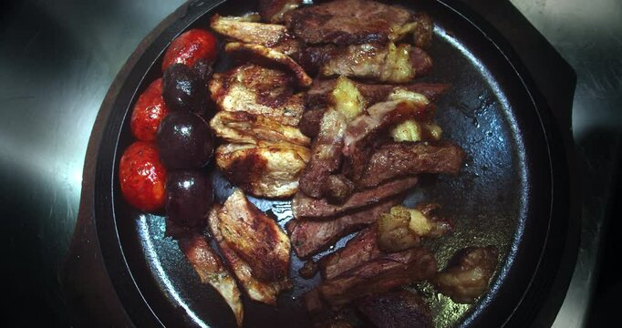 Beautiful slow motion, overhead angle shot of a large grill plate with roast beef, chorizo, potatoes and roast chicken inside a restaurant kitchen.