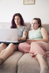 Obraz premium Two women sitting on a couch looking at a laptop