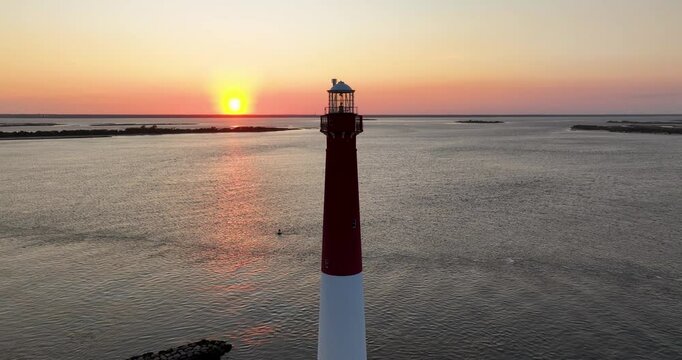 A 24mm Wide-angle drone shot of the Barnegat Lighthouse, located in Long Beach Island, New Jersey. The camera orbits around the lighthouse, with the sunset perfectly aligned as it passes through.