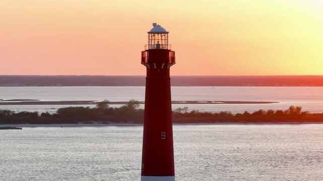 A 166mm Tele-Camera drone shot of the Barnegat Lighthouse, located in Long Beach Island, New Jersey. The camera focuses in on the top half of the structure, while the sunset passes in the background.