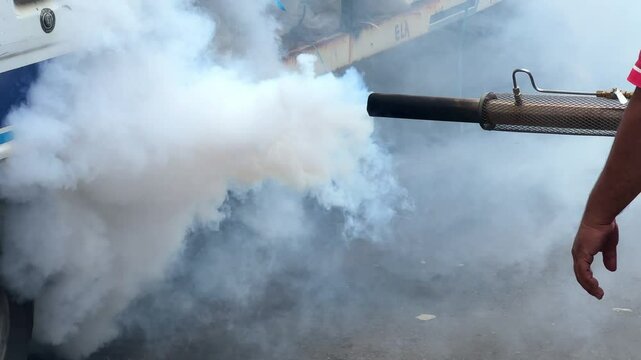 A person with a smoke-producing machine used to exterminate mosquitoes