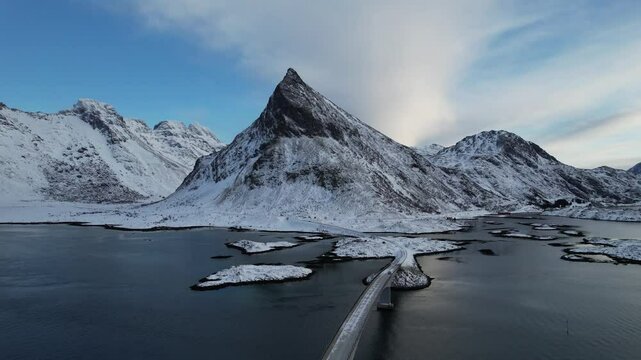 Aerial view of fredvang bridge surrounded by snowy mountains and serene sea, lofoten, norway.