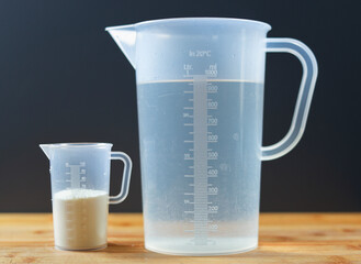 A measuring cup with water and a small measuring cup with milk powder.