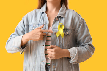 Woman pointing at yellow awareness ribbon on color background, closeup