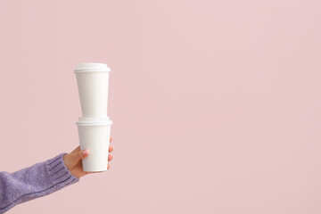 Female hand with takeaway paper cups on purple background