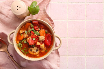 Pot of tasty beef stew on pink tile background