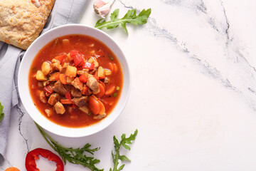 Bowl of tasty beef stew on white marble background