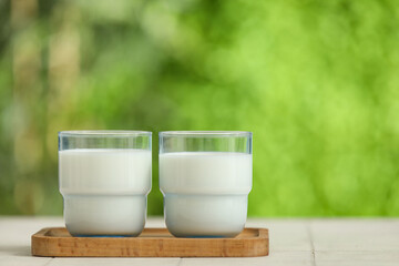 Wooden board with glasses of fresh milk on white tile table outdoors