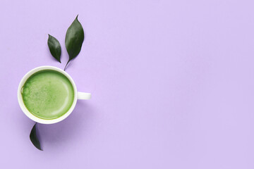 Cup of fresh matcha tea and plant leaves on lilac background