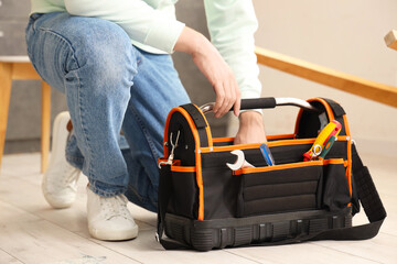 Young man with bag of tools assembling furniture in kitchen, closeup