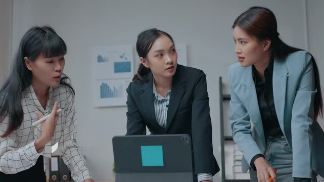 Three businesswomen engage in a heated discussion about work while focusing on a laptop during a business meeting, showcasing their strong emotions and professional dynamics