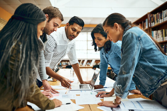 Library, university student and group work with laptop for research, teamwork and collaboration on campus. People, classmates and college learner with document or notes for test, study and exams