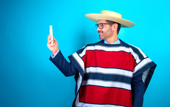 retrato hombre maduro vestido con ropa tradicional huaso chileno sosteniendo y mirando el celular, fondo azul estudio 